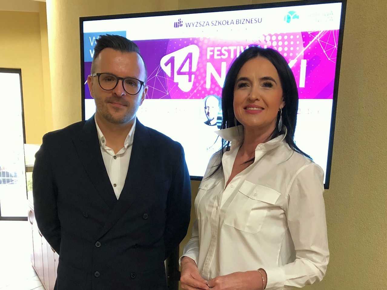 Dwójka ludzi stoi obok ekranu z informacjami o festiwalu nauki.