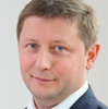 Mężczyzna w garniturze z krótkimi włosami, uśmiechający się lekko.