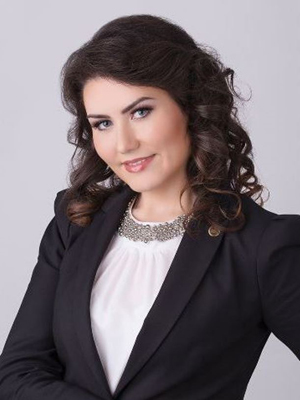 Kobieta w eleganckim garniturze, z uśmiechem i kręconymi włosami.