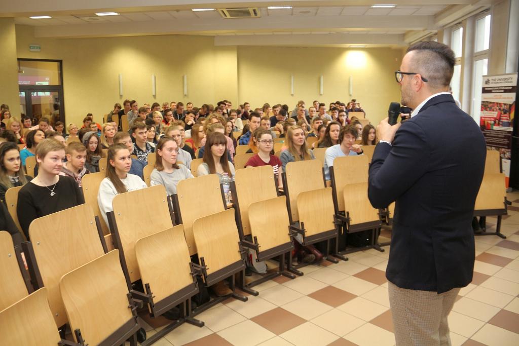 Dwóch mężczyzn prowadzi wykład przed dużą grupą słuchaczy w sali wykładowej.