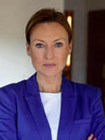 Kobieta w niebieskim żakiecie, z założonymi rękami, patrząca w stronę kamery.
