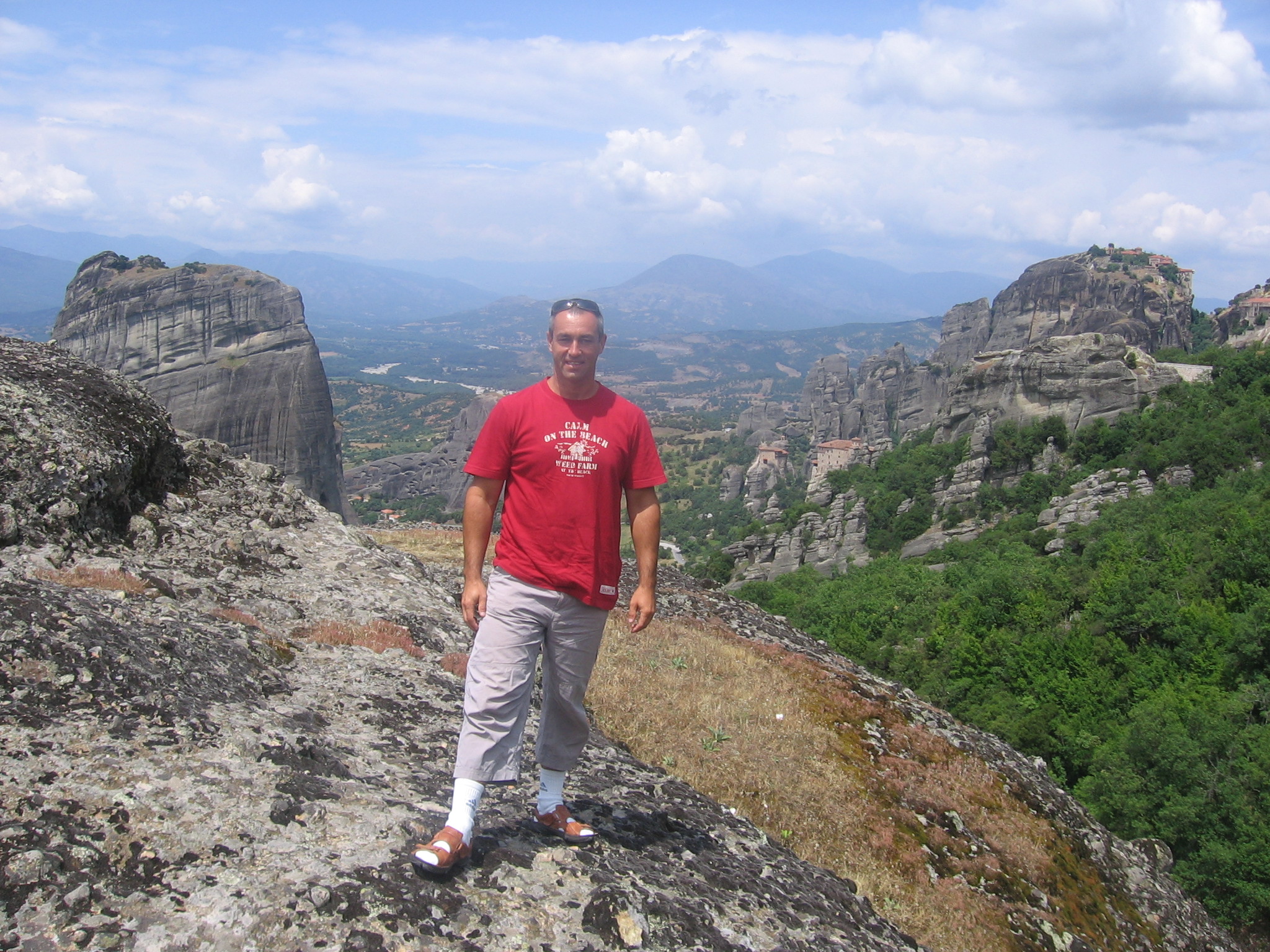 Mężczyzna stoi na skalnym wzniesieniu z widokiem na górzysty krajobraz.