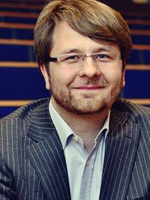 Mężczyzna w okularach, uśmiechający się, ubrany w garnitur.