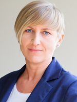 Kobieta z krótkimi blond włosami, ubrana w granatową marynarkę, patrzy w stronę obiektywu.