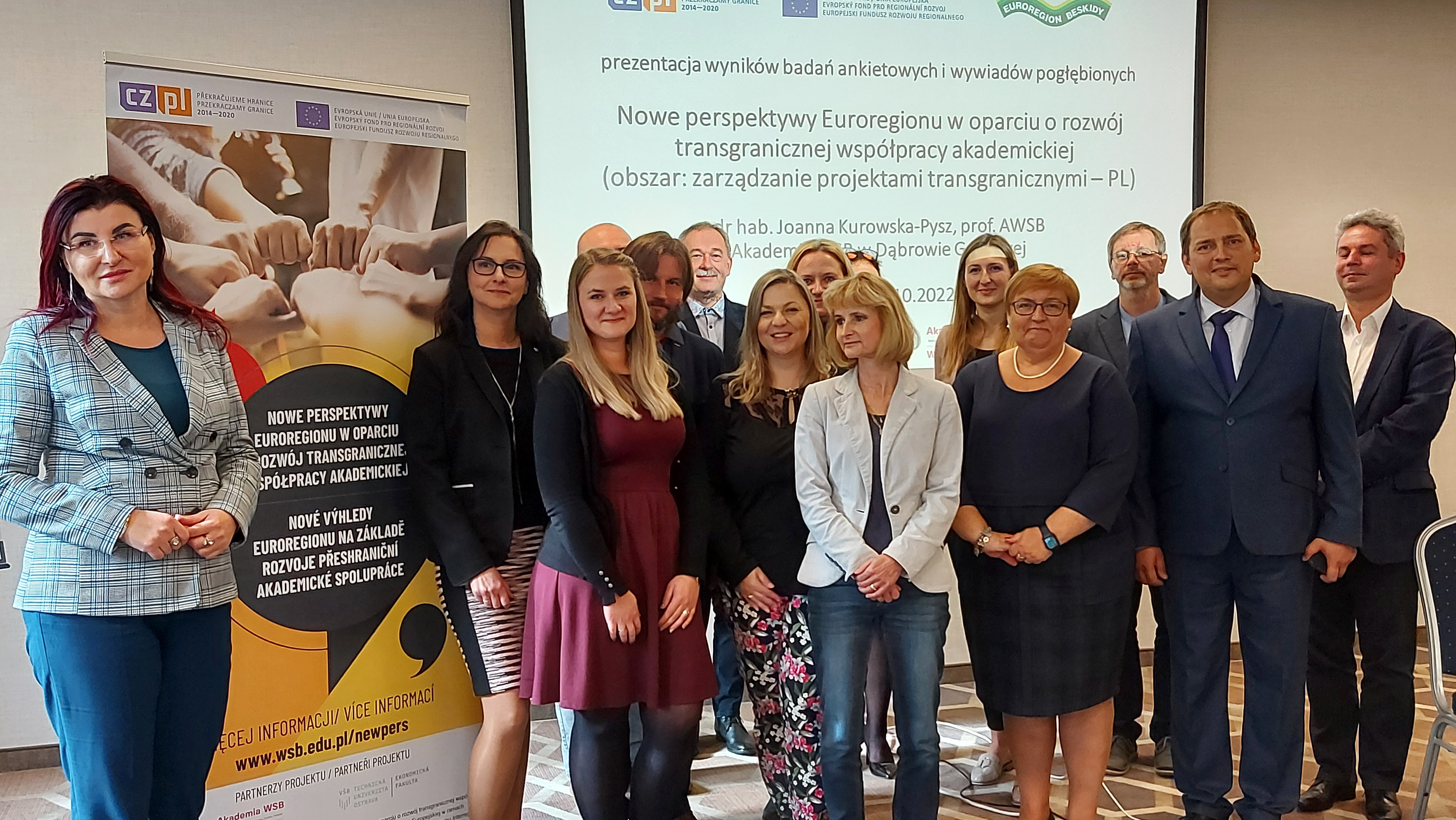 Grupa osób stoi przed prezentacją na temat nowych perspektyw Euroregionu, związanych z transgraniczną współpracą akademicką.