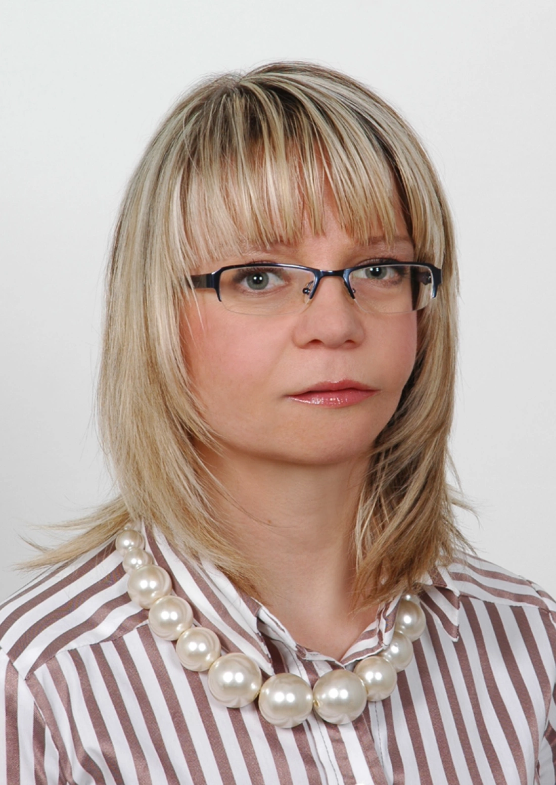 Zdjęcie kobiety w klasycznej bluzce w paski, noszącej okulary i dużą perłową naszyjnik.