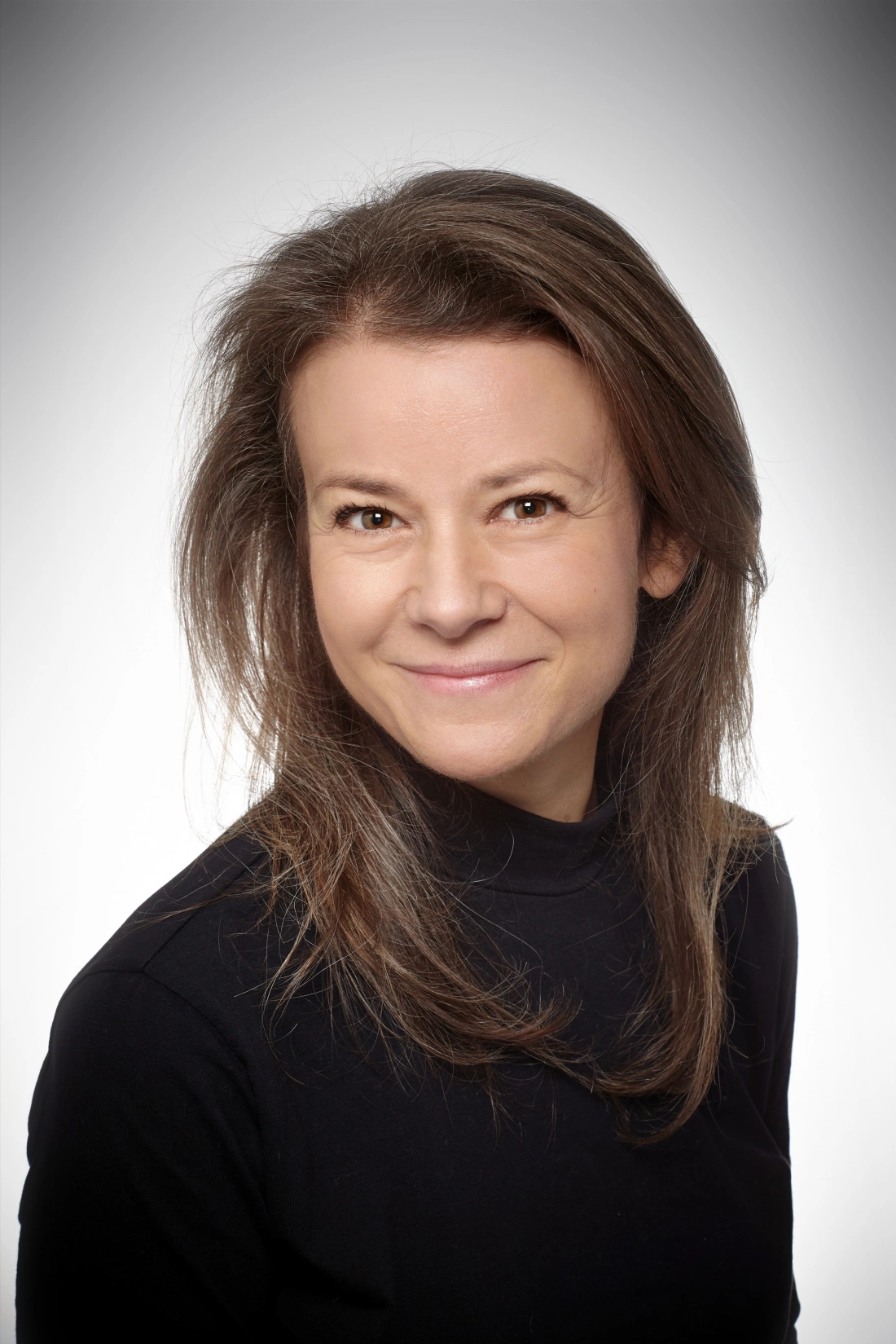 Portret uśmiechającej się kobiety z długimi włosami, ubranej w czarny sweter.