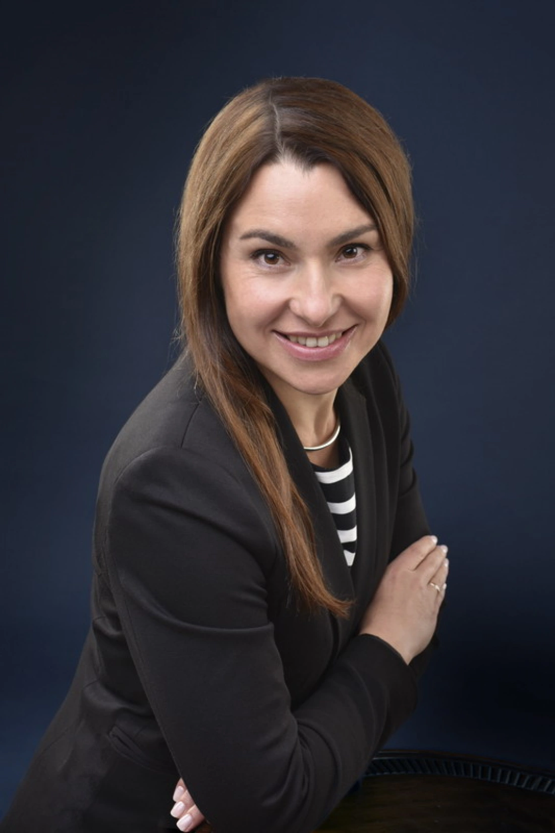 Młoda kobieta w żakiecie, uśmiechając się i pozując na ciemnym tle.