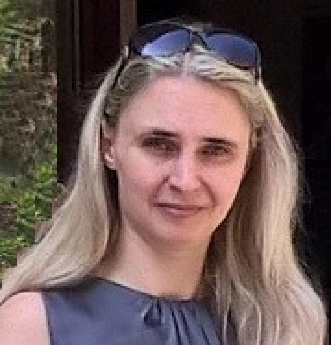 Kobieta z długimi, jasnymi włosami, w okularach przeciwsłonecznych, w eleganckiej bluzce.