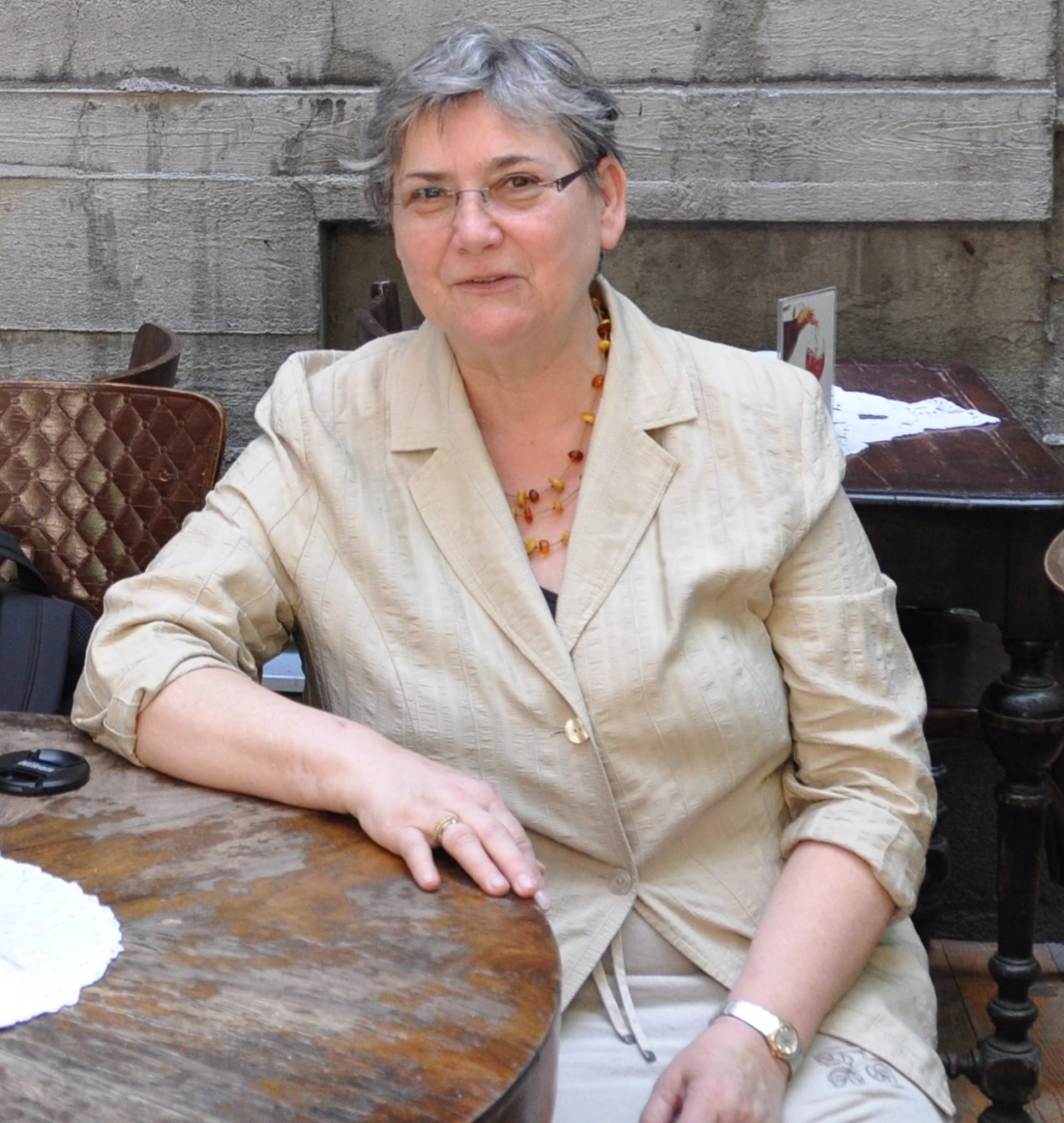 Kobieta w jasnej marynarce siedzi przy drewnianym stole.