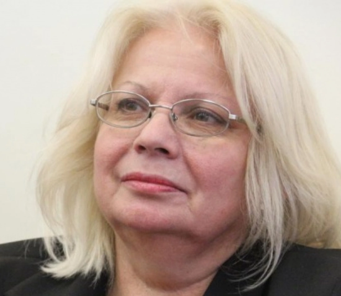 Kobieta z długimi, jasnymi włosami, w okularach, wygląda na zamyśloną.