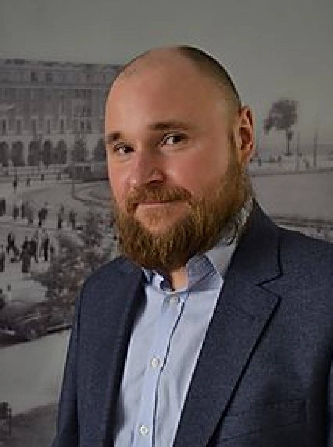 Mężczyzna z brodą w eleganckim garniturze, z tłem w stylu vintage.