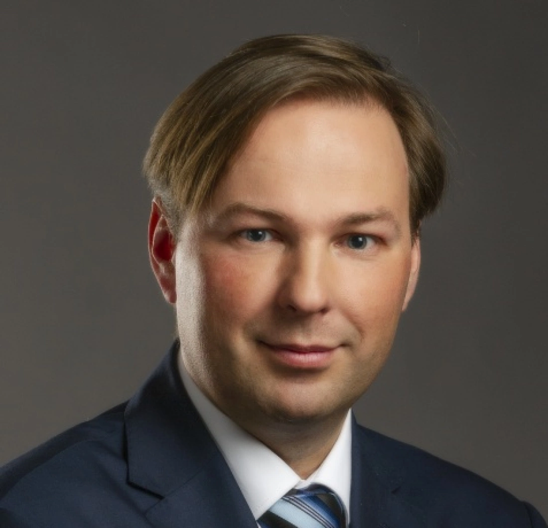 Portret mężczyzny w garniturze, z gładko ułożonymi włosami i poważnym wyrazem twarzy.