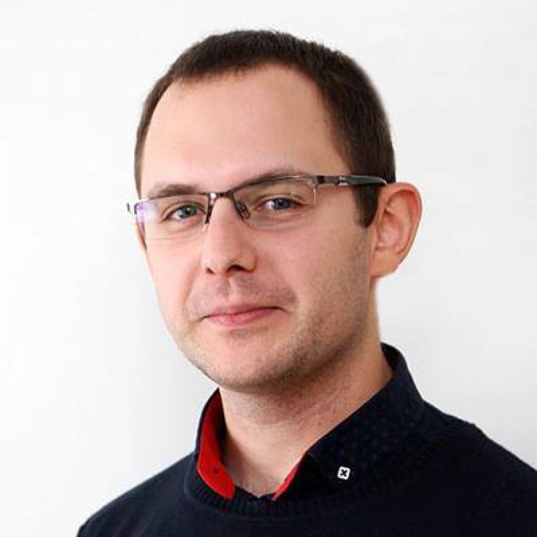 Mężczyzna w okularach, z uśmiechem, ubrany w ciemny sweter.