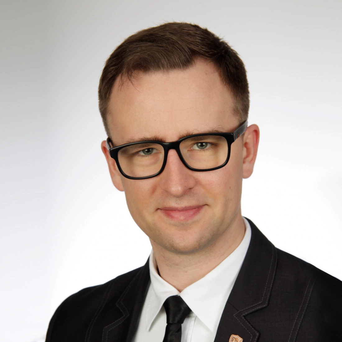 Mężczyzna w eleganckim garniturze z okularami, uśmiechający się do kamery.