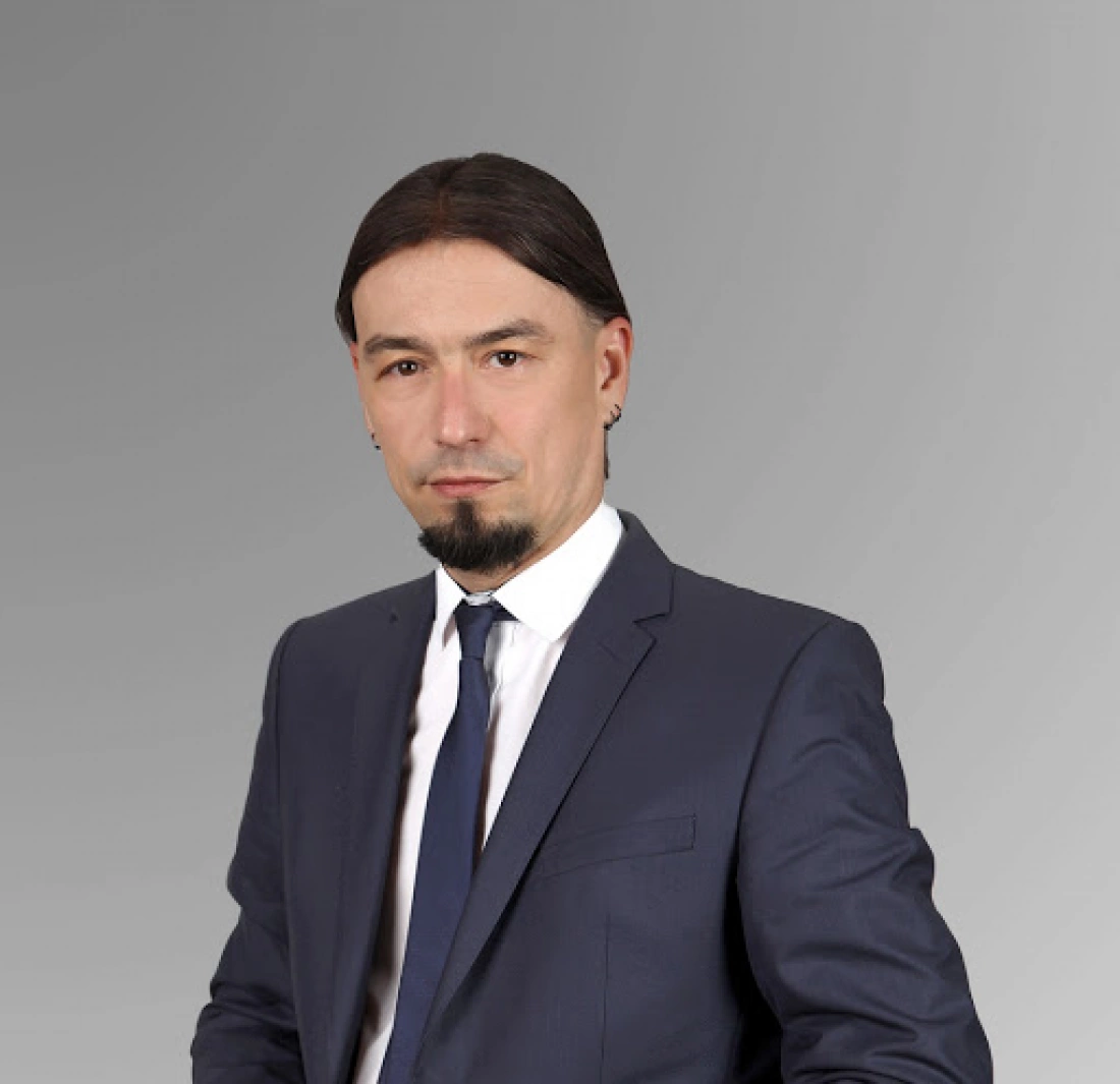 Mężczyzna w garniturze z eleganckim krawatem, pozujący na neutralnym tle.