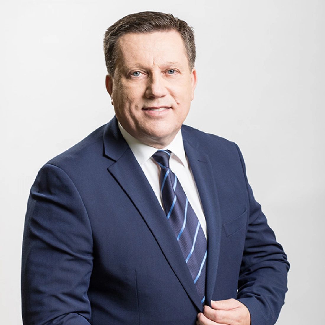 Mężczyzna w garniturze, uśmiechający się do aparatu na jasnym tle.