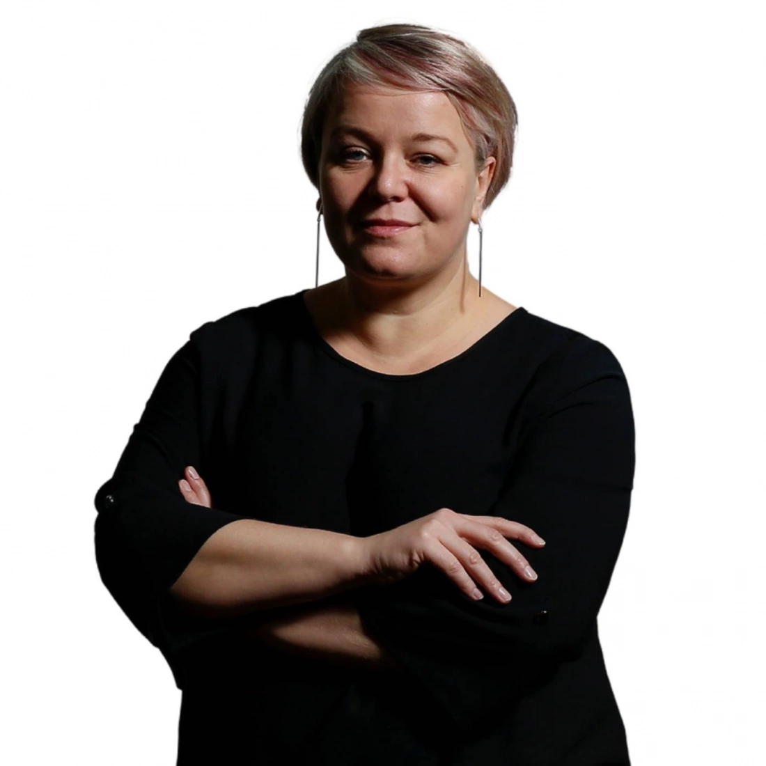 Kobieta z krótkimi włosami, ubrana w czarną bluzkę, stoi z założonymi rękami.
