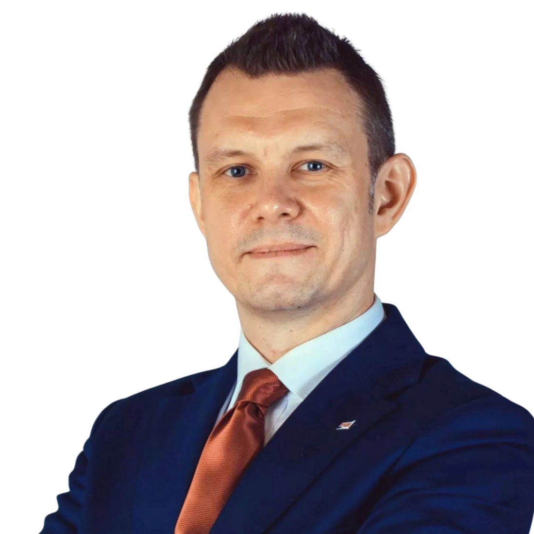 Mężczyzna w garniturze z uśmiechem, z rękami skrzyżowanymi na piersi.