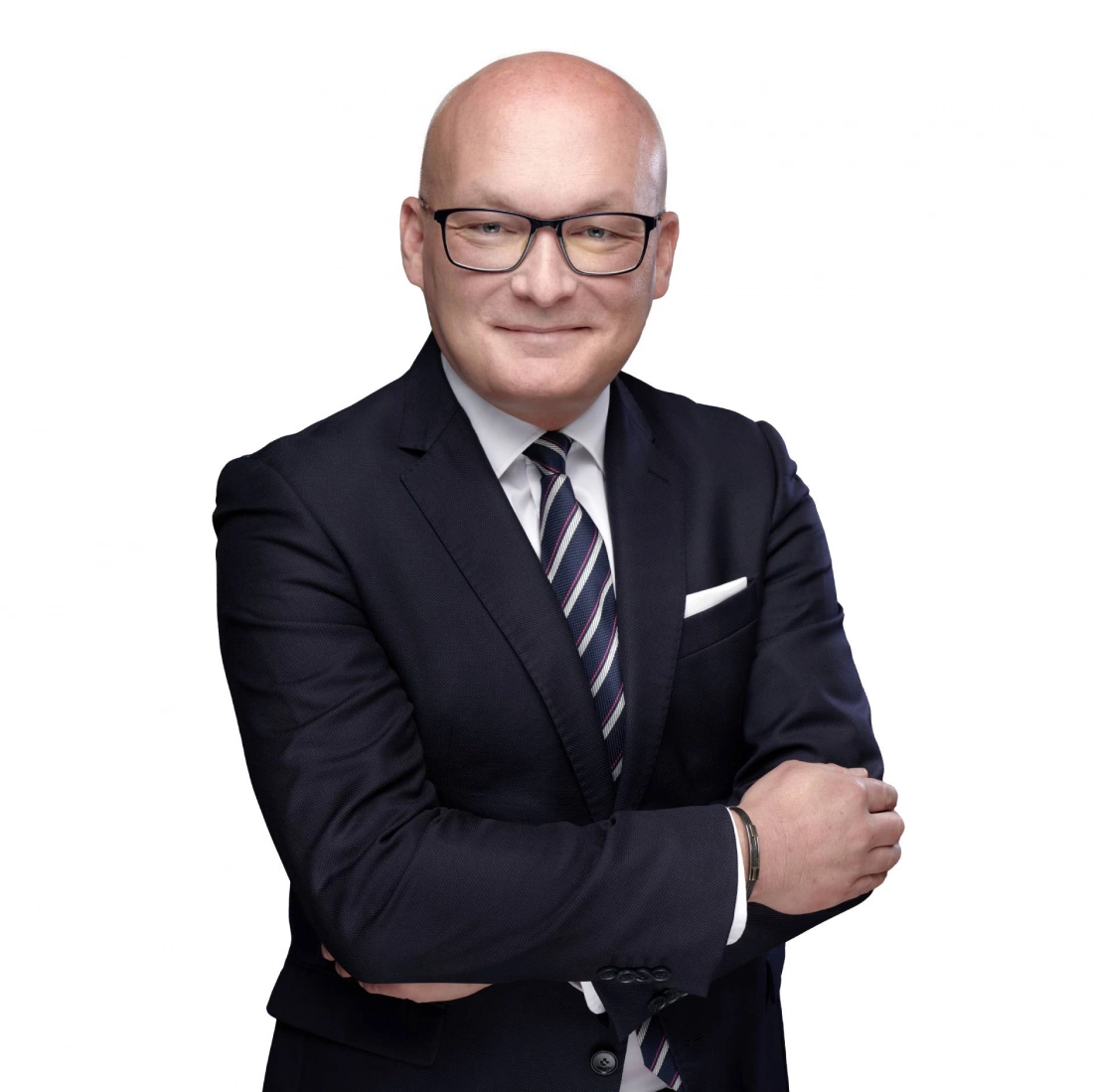 Mężczyzna w eleganckim garniturze z założonymi rękami, uśmiechający się.