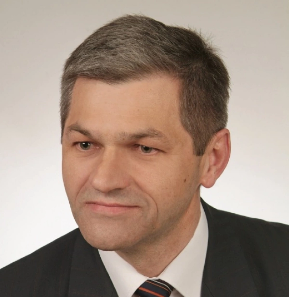 Mężczyzna w eleganckim garniturze, z krótkimi szarymi włosami, ujęty w zbliżeniu.