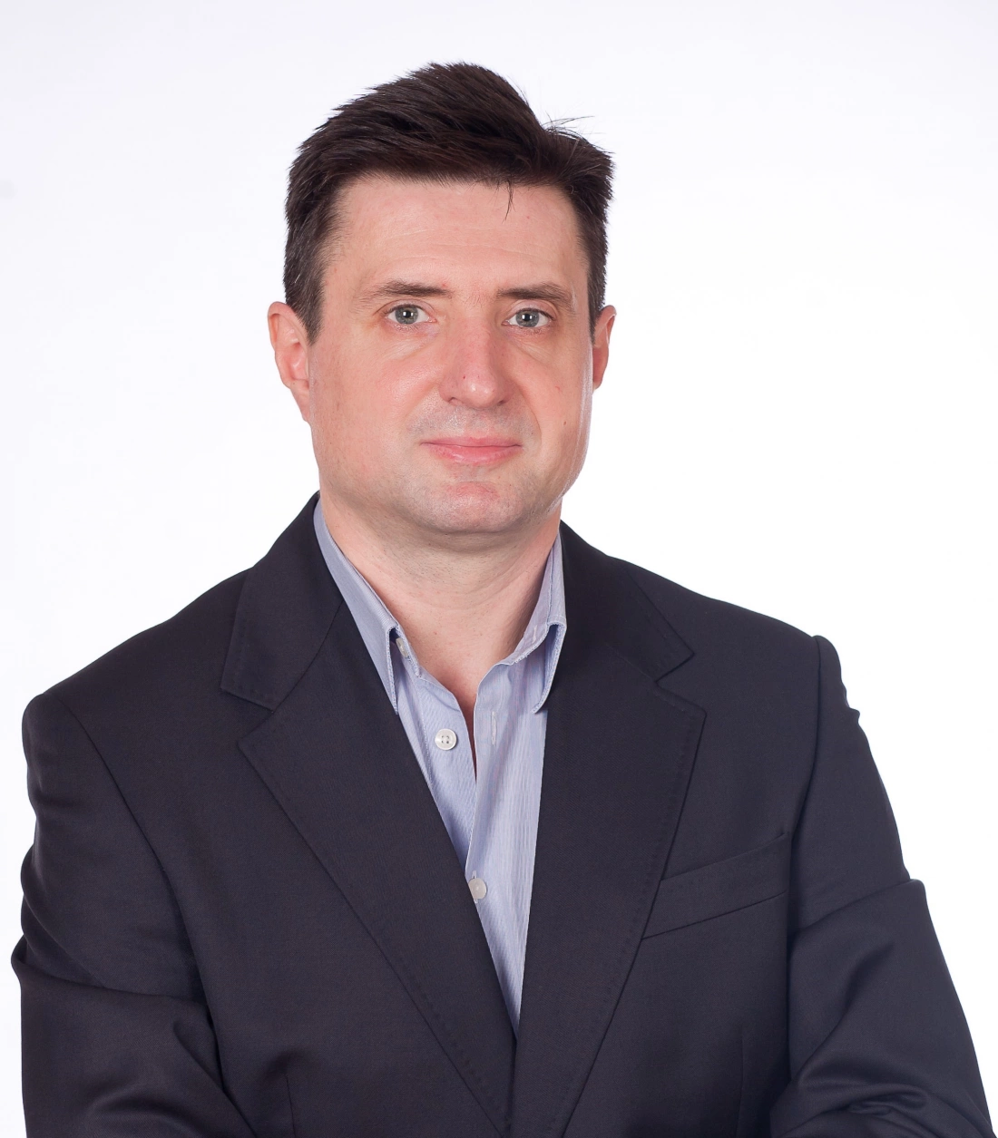 Mężczyzna w garniturze, z krótkimi włosami, stojący na jasnym tle.