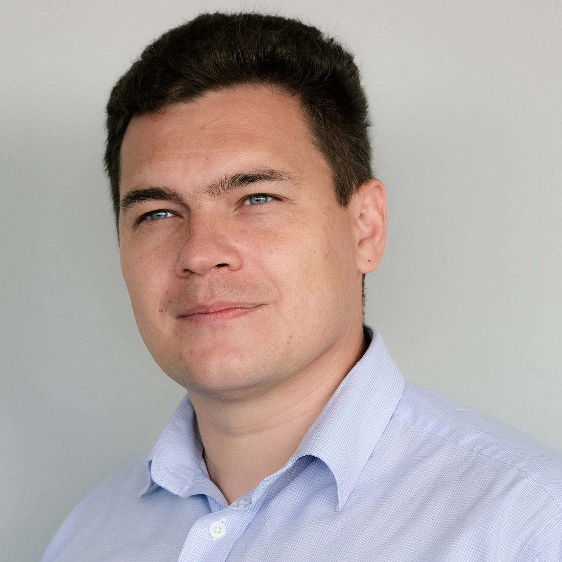 Mężczyzna z krótkimi włosami, uśmiechający się w kierunku kamery, ubrany w jasną koszulę.