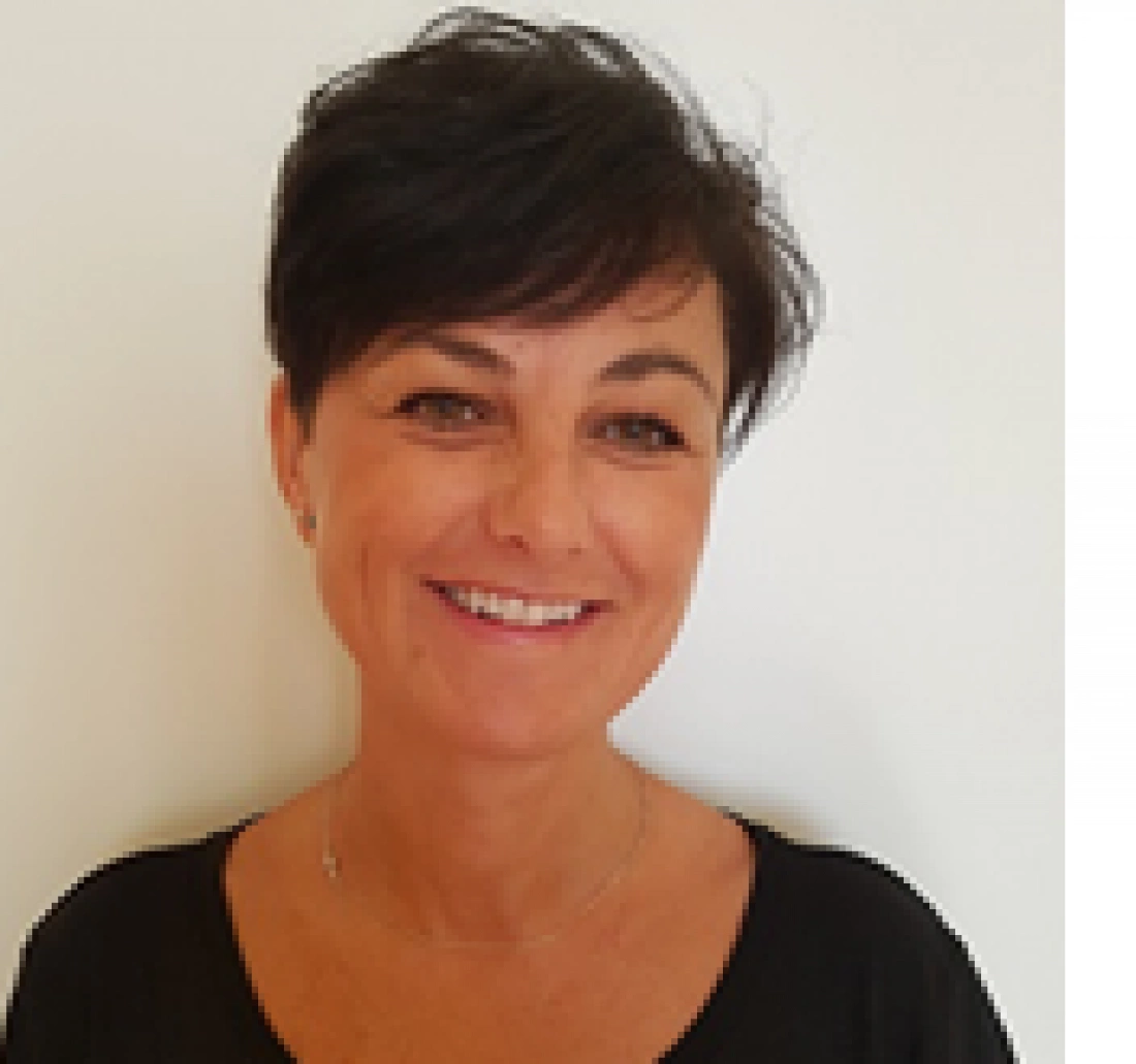 Kobieta z uśmiechem, krótkie ciemne włosy, neutralne tło.