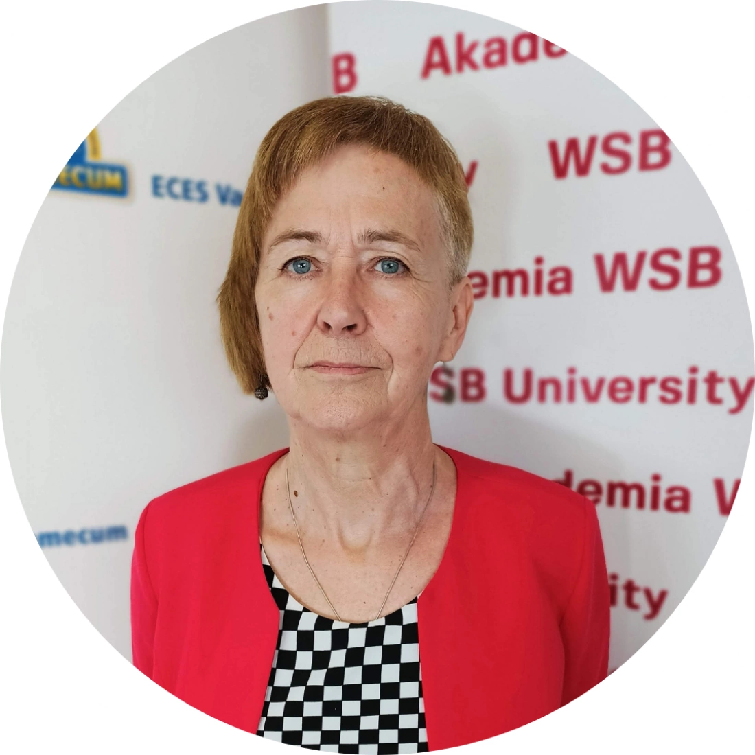 Portret kobiety w czerwonej marynarce z krótkimi włosami, stojącej przed tłem z logo uczelni.