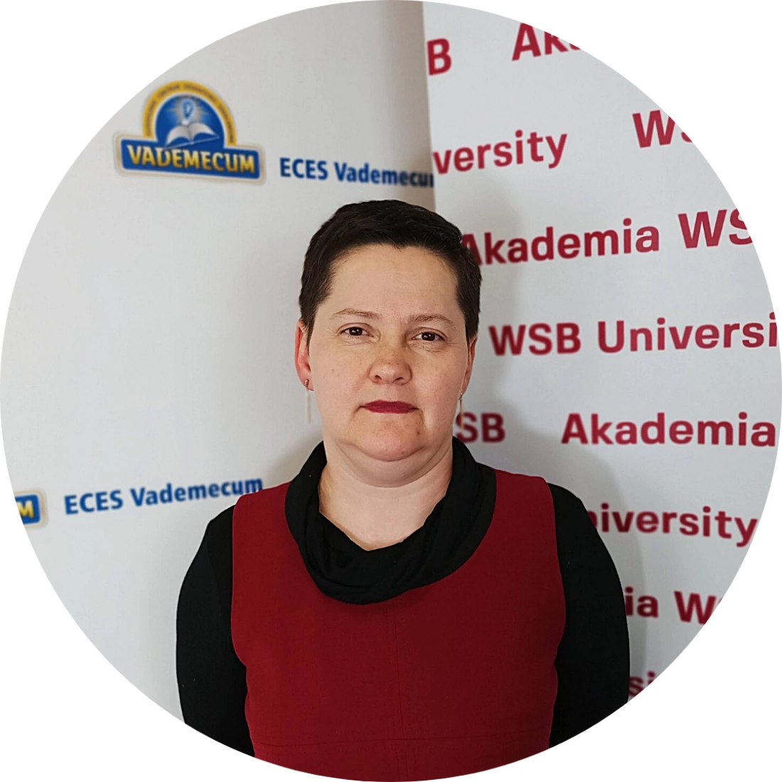 Kobieta w czerwonej sukience stoi przed tłem z logotypami Akademii WSB i Vademecum.