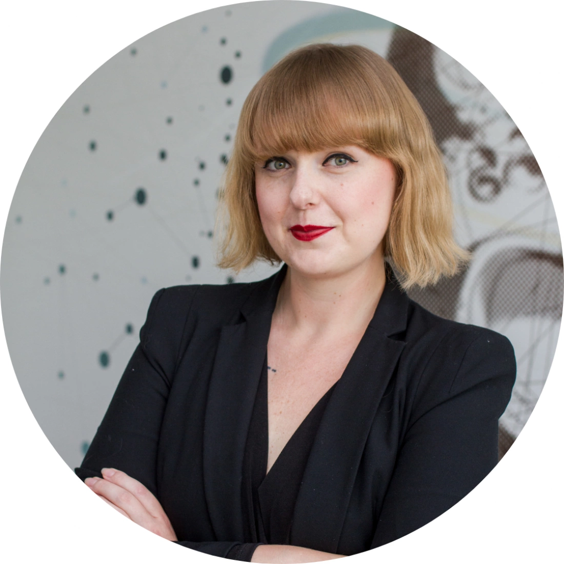 Kobieta o krótkich, blond włosach w czarnej marynarce, z założonymi rękoma na tle nowoczesnego wzoru.