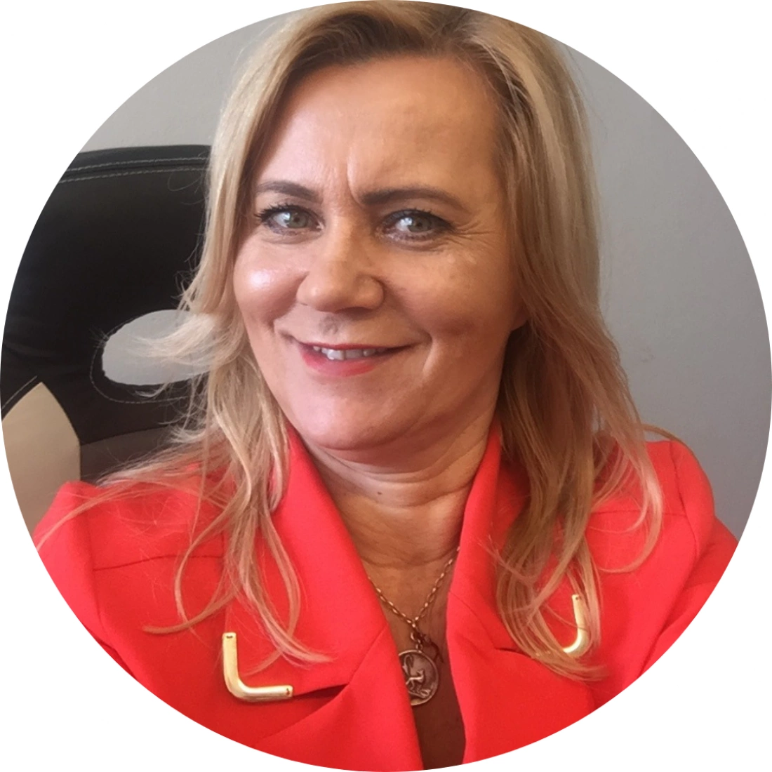 Kobieta w jasnoróżowej marynarce uśmiecha się do aparatu, siedząc na tle biurowego krzesła.