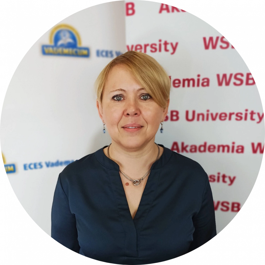 Kobieta w niebieskiej bluzce stoi przed tłem z napisami "Akademia WSB".