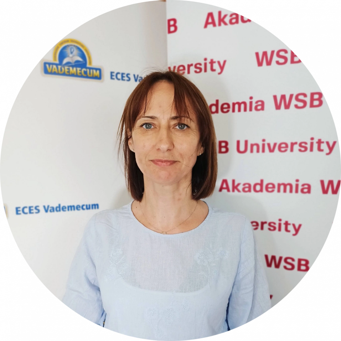 Kobieta w jasnej bluzce stoi na tle bannerów Akademii WSB i ECES Vademecum.