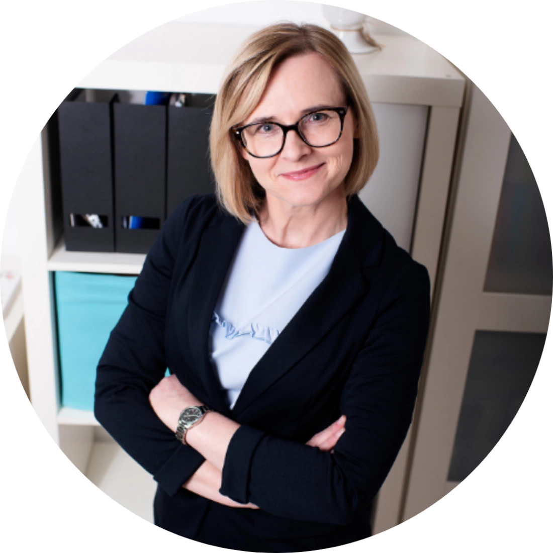 Kobieta w eleganckim ubraniu z założonymi rękami, uśmiechająca się w biurze.