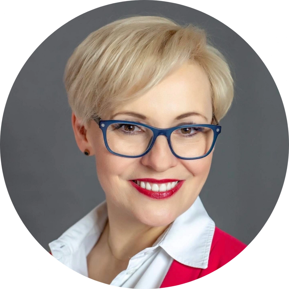 Portret uśmiechniętej kobiety w okularach, z krótkimi, jasnymi włosami.