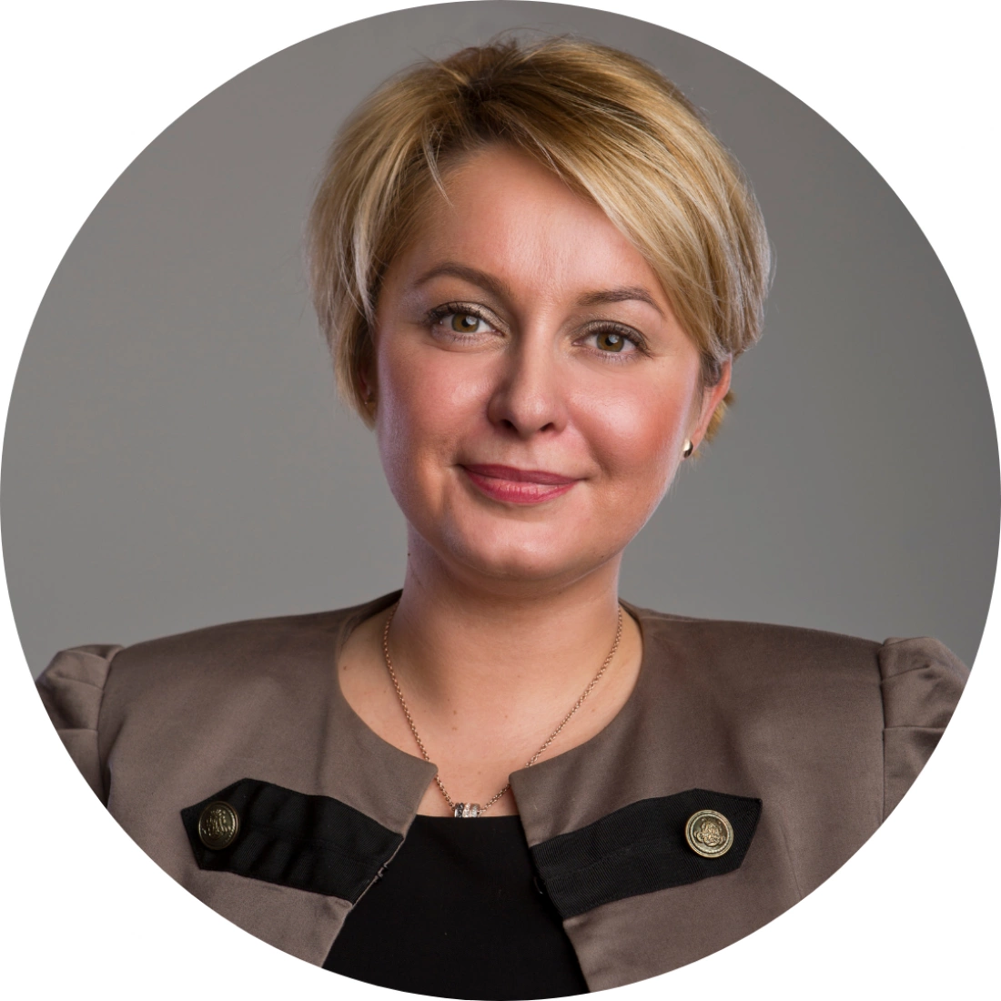 Portret kobiety z krótkimi blond włosami, uśmiechającej się w eleganckim stroju.