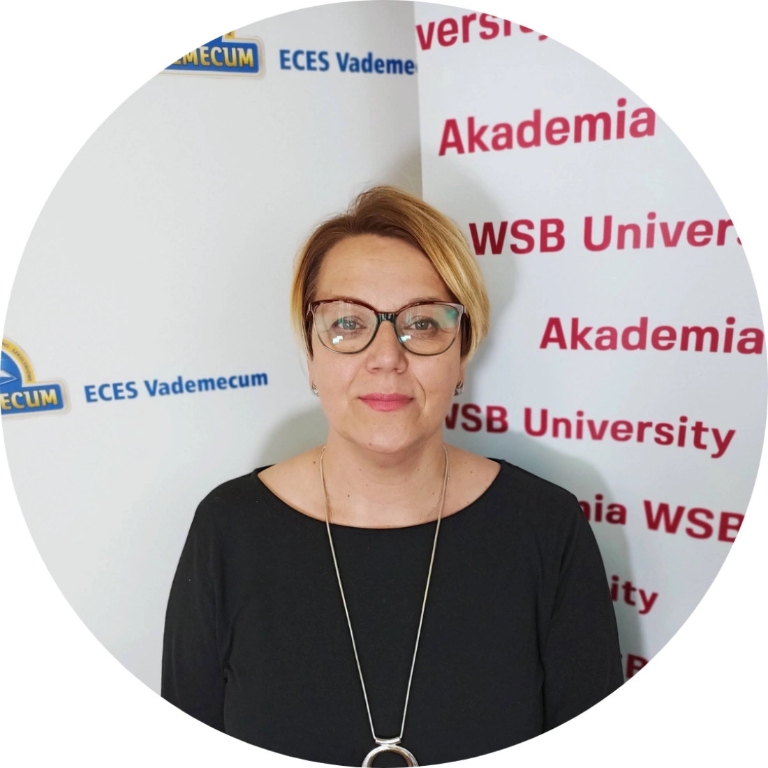Kobieta w okularach stoi na tle bannerów uczelni.