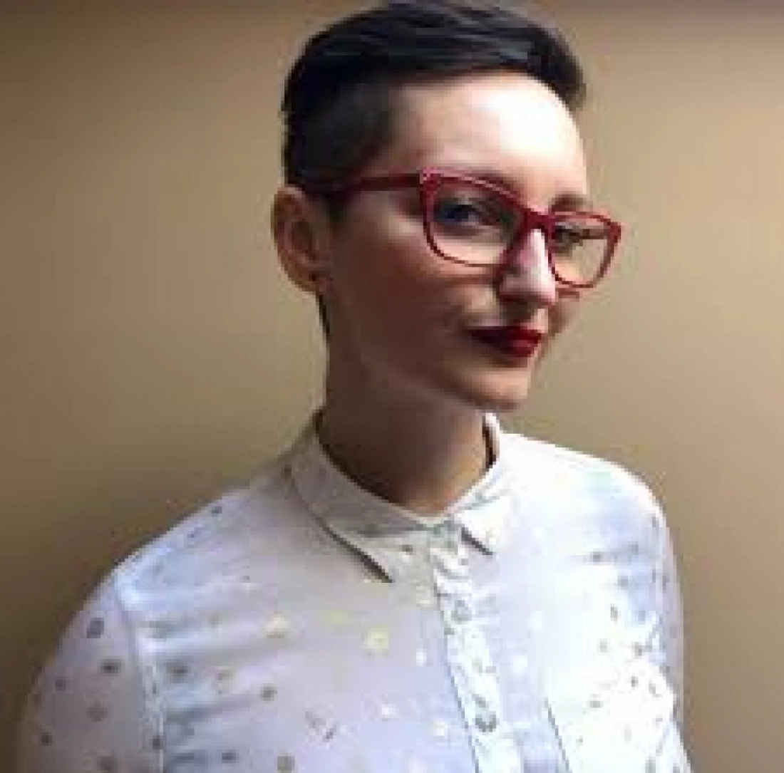 Osoba z krótkimi włosami, w okularach i białej koszuli, z delikatnym uśmiechem.