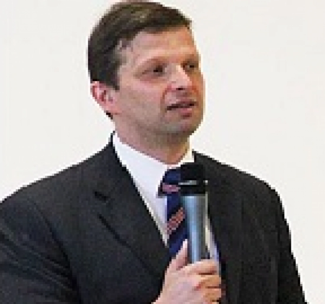 Mężczyzna w garniturze trzyma mikrofon i mówi.