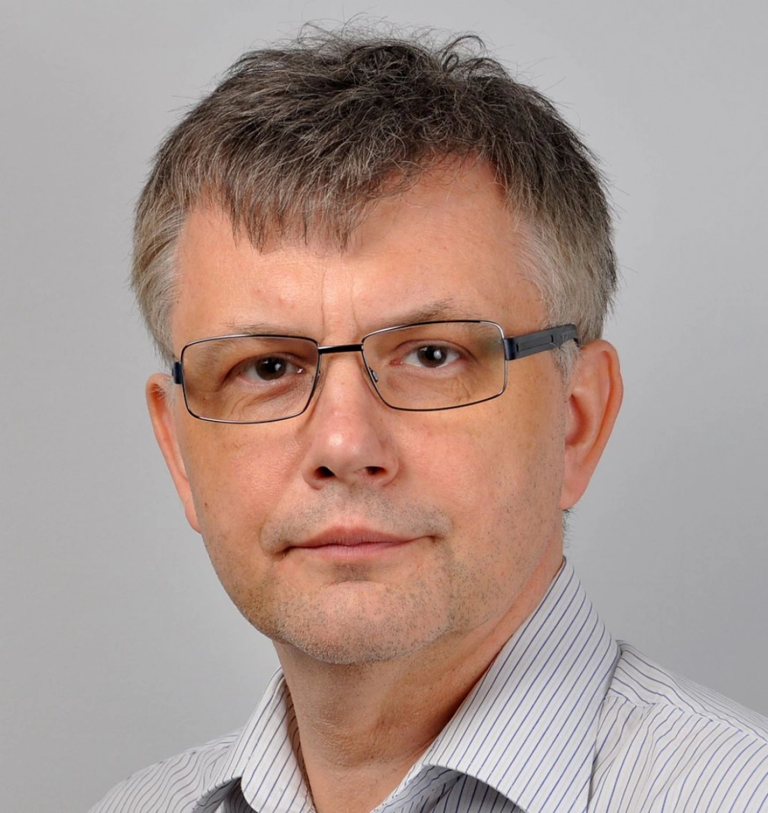 Mężczyzna w okularach z krótkimi włosami, na jasnym tle.
