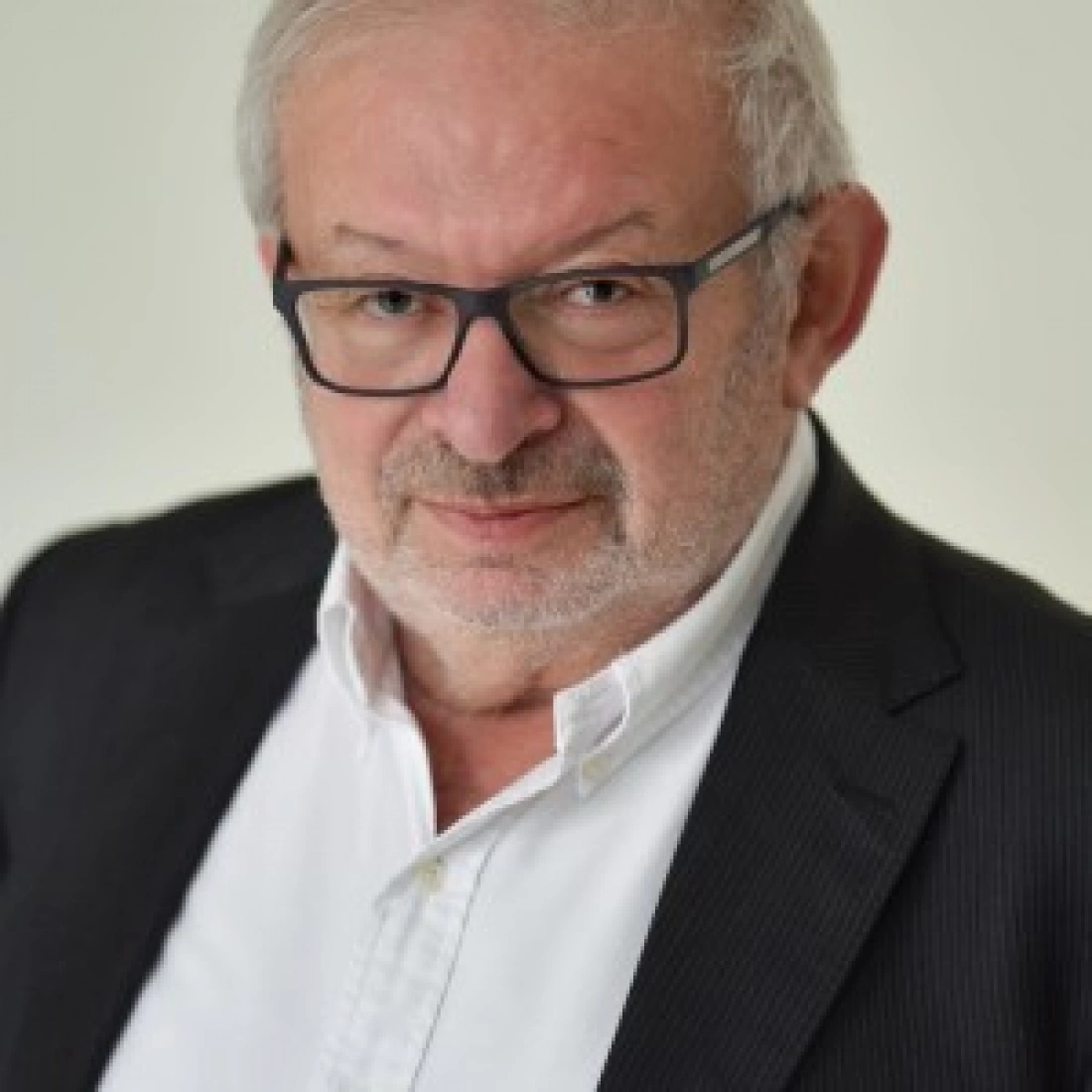 Mężczyzna w okularach, ubrany w garnitur, z poważnym wyrazem twarzy.