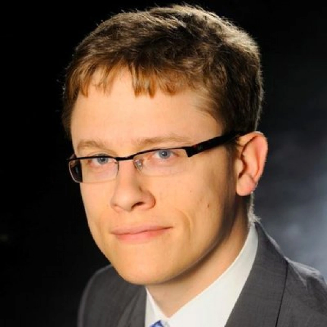 Mężczyzna z okulary w garniturze, uśmiechający się do kamery.