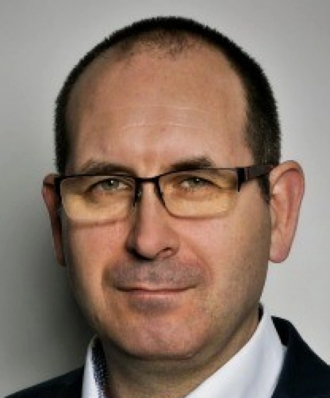 Mężczyzna w okularach, uśmiechający się lekko, na neutralnym tle.