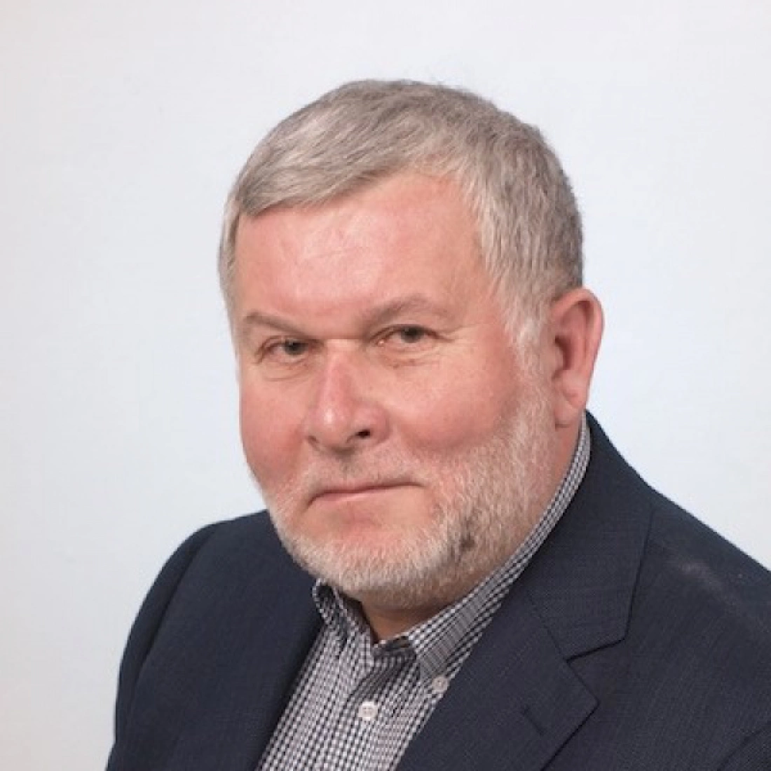 Mężczyzna w ciemnym garniturze z siwą brodą, patrzący w kamerę.