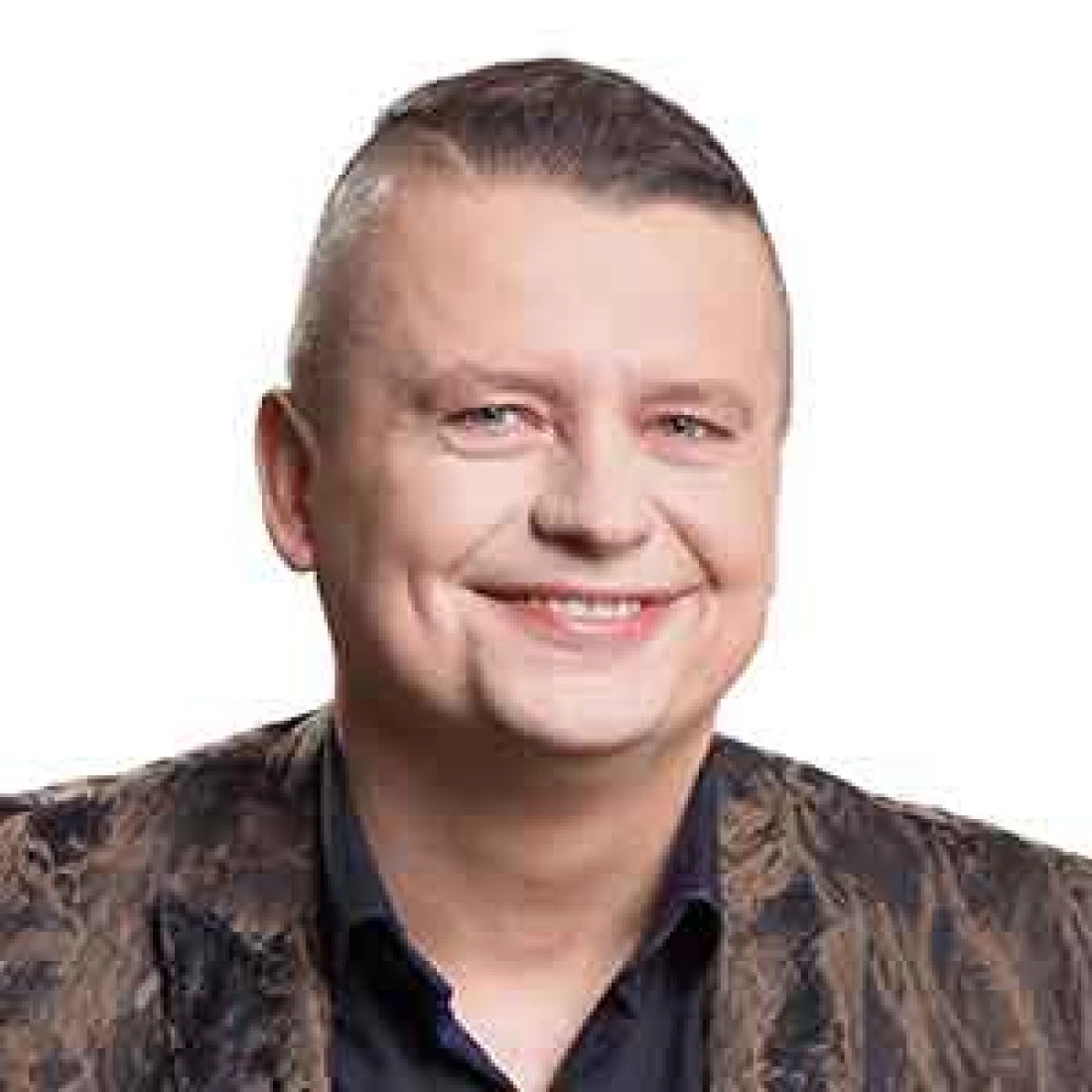 Mężczyzna z uśmiechem, w eleganckiej koszuli i kamizelce, na tle białym.