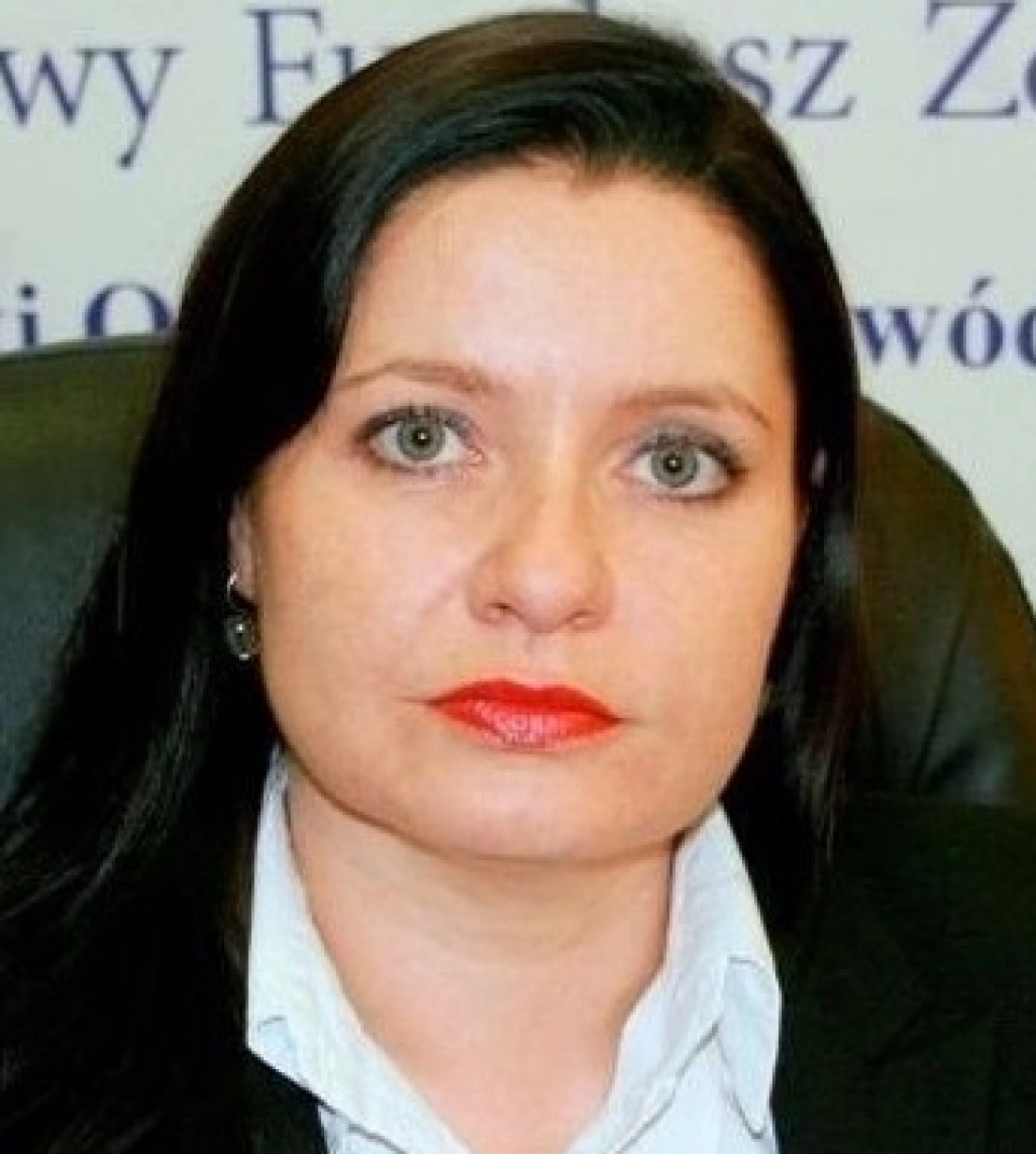 Kobieta z długimi, ciemnymi włosami i zielonymi oczami, ubrana w białą koszulę i czarną marynarkę.