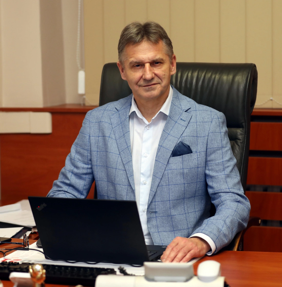 Mężczyzna w niebieskim garniturze siedzi przy biurku z laptopem.