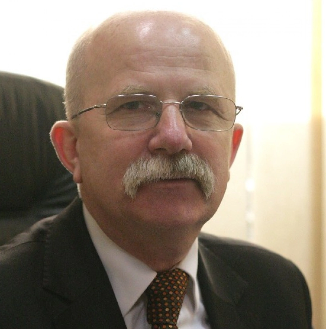 Mężczyzna z okularami i wąsami, siedzący w biurze.