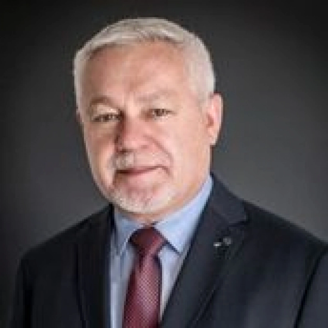 Mężczyzna w garniturze, na tle ciemnego tła, z uśmiechem na twarzy.